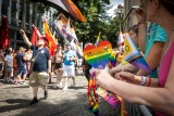 Man sieht eine Parade bunt gekleideter Menschen beim Christopher Street Day. Auf beiden Seiten stehen Menschen, die die Parade anschauen.