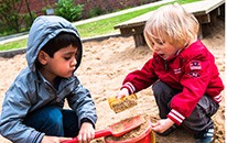 Zwei Kleinkinder spielen in einem Sandkasten. 