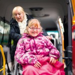 Ein Kind im Rollstuhl wird in einen Wagen gehoben. 